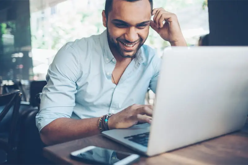 A man smiles while working on his laptop, conveying a sense of enjoyment and engagement with his task.